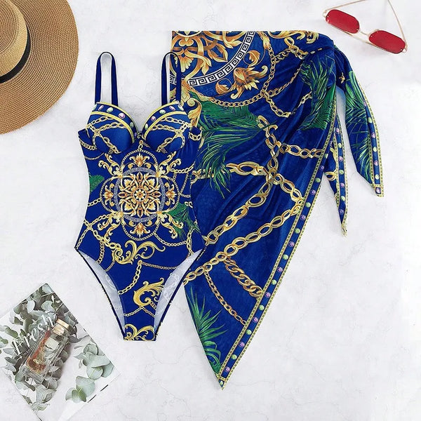 Blauw badpak met gouden ketting- en palmbladprint, bijpassende sarong, zonnebril en hoed. Perfect voor strandmode en zomerstijl.