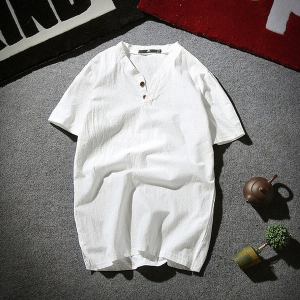Witte linnen heren T-shirt met korte mouwen en knoopsluiting, casual zomerstijl, liggend op grijze vloer met theepot en plantdecoratie.