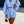 Vrouw in lichtblauwe zomerset met pofmouwen en korte broek, draagt een kleine bruine handtas. Trendy damesmode, casual outfit.