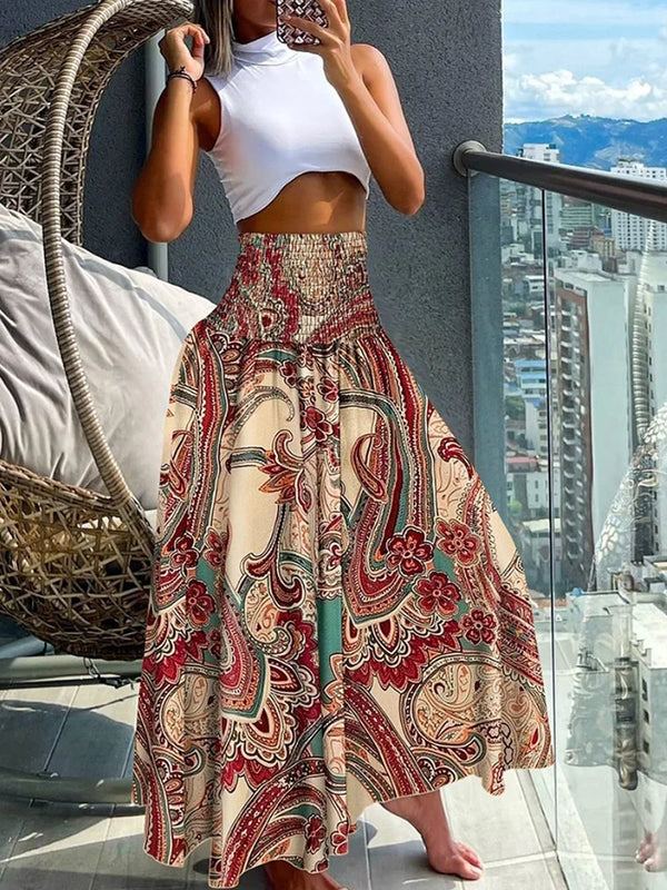 Vrouw in witte crop top en kleurrijke bohemian maxi-rok met paisley-patroon, staand op balkon met stadzicht. Zomermode, boho-chic stijl.