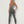 Vrouw in grijze sportlegging en top, fitnesskleding, rugaanzicht, staand tegen witte achtergrond, sportmode, actieve levensstijl.
