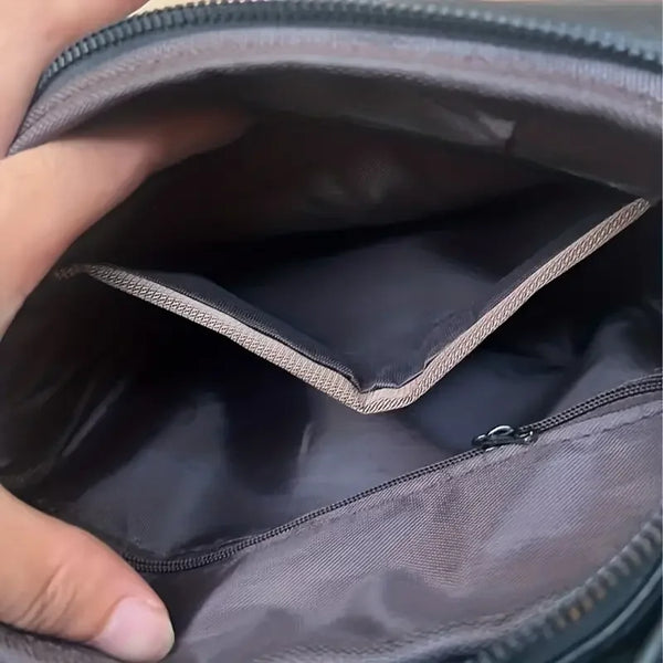Hand houdt open zwarte leren tas met meerdere vakken en rits, ideaal voor damesmode, accessoires en organisatie. Ruime binnenkant zichtbaar.