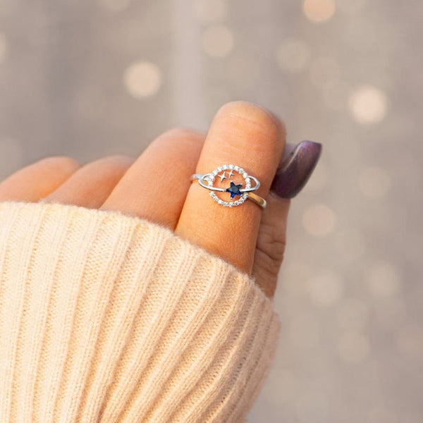 Zilveren ring met blauwe ster en kristallen op een hand met beige trui. Modieuze sieraden, elegante damesring, trendy accessoires.