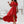 Elegante vrouw in rode off-shoulder jurk met ruches, staand in moderne woonkamer. Trendy mode, zomerjurk, stijlvolle outfit.