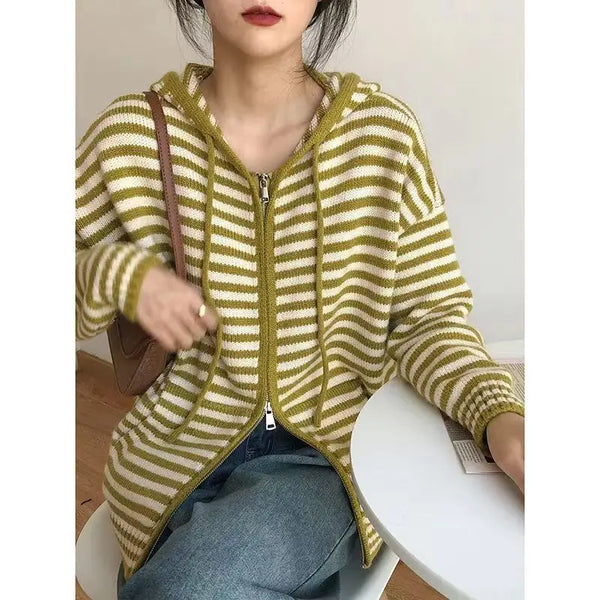 Vrouw draagt gestreepte groene en witte hoodie met rits, zittend aan tafel. Modieuze casual dameskleding, comfortabele herfstoutfit.