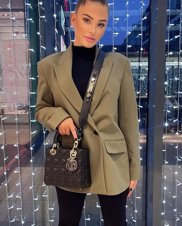 Vrouw met groene blazer en zwarte handtas voor verlichte achtergrond, stijlvolle mode, moderne outfit, avondlook.