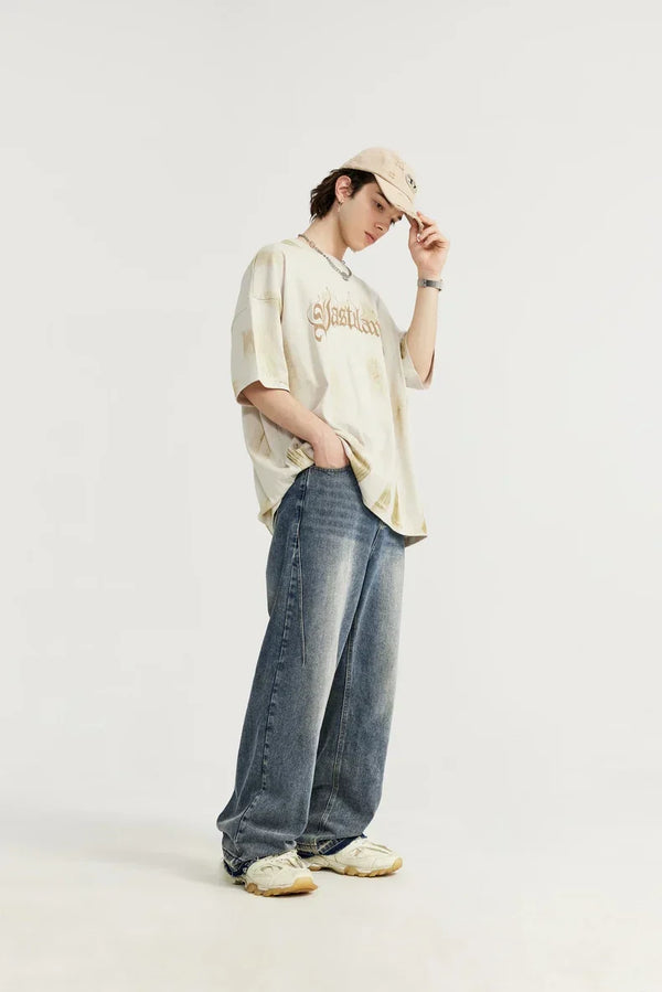 Jonge man in oversized beige T-shirt en wijde jeans, draagt een beige pet en sneakers. Casual streetwear mode, trendy outfit voor jongeren.