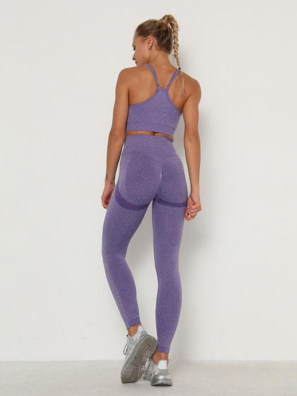 Vrouw in paarse sportkleding, bestaande uit een sportbeha en legging, poseert tegen een witte achtergrond. Fitnessmode, actieve kleding, sportoutfit.