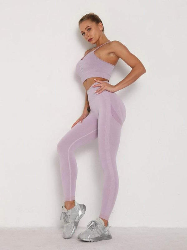 Vrouw in lila sportset, bestaande uit een crop top en leggings, poseert tegen een witte achtergrond. Dames sportkleding, fitnessmode, actieve stijl.