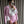 Vrouw in roze pied-de-poule pak met witte blouse en veren, houdt roze mini-handtas en smartphone vast, draagt zonnebril en scrunchie.