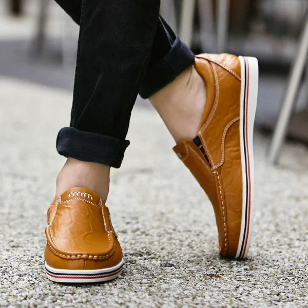 Bruine leren loafers voor heren, casual stijl, gedragen met opgerolde zwarte jeans. Comfortabele schoenen met witte zool en stikseldetails.