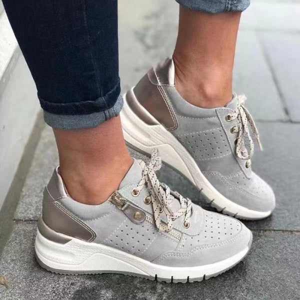 Grijze dames sneakers met dikke zool, perforaties en veters, gedragen met donkere jeans. Comfortabele en modieuze schoenen voor dagelijks gebruik.