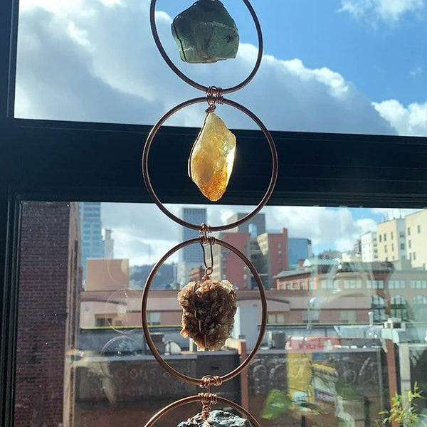 Drie kristallen in koperen ringen voor een raam met stadszicht; groene, gele en bruine kristallen. Perfect voor interieurdecoratie en spirituele energie.