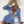 Vrouw in blauwe gestreepte strandjurk en bikini, met witte hoed en smartphone, zittend op witte bank. Zomermode, strandkleding, trendy outfit.