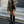 Vrouw in stijlvolle herfstoutfit met olijfgroene blazer, zwarte rok met split, hoge laarzen en kleine schoudertas, staand op stenen trap.