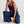 Vrouw in blauwe jumpsuit, zittend op witte achtergrond. Modieuze dameskleding, casual stijl, comfortabele pasvorm, trendy outfit.