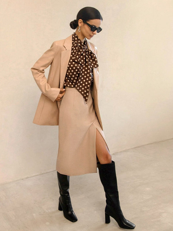 Elegante vrouw in beige blazer en rok met bruine stippenblouse, zwarte laarzen en zonnebril. Modieuze dameskleding, herfststijl.