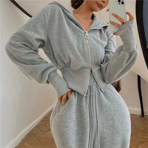 Vrouw in grijze joggingpak met capuchon, rits en zakken, poseert binnenshuis. Comfortabele loungewear, modieuze sportkleding, casual stijl.