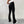 Vrouw in zwarte flared broek en witte sneakers tegen een grijze achtergrond. Modieuze dameskleding, casual outfit, trendy stijl.