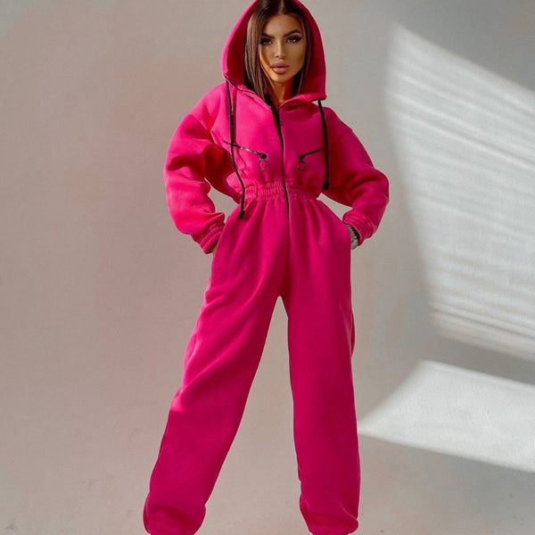 Vrouw in felroze joggingpak met capuchon, poseert tegen een neutrale achtergrond. Modieuze dameskleding, comfortabele streetwear, trendy outfit.