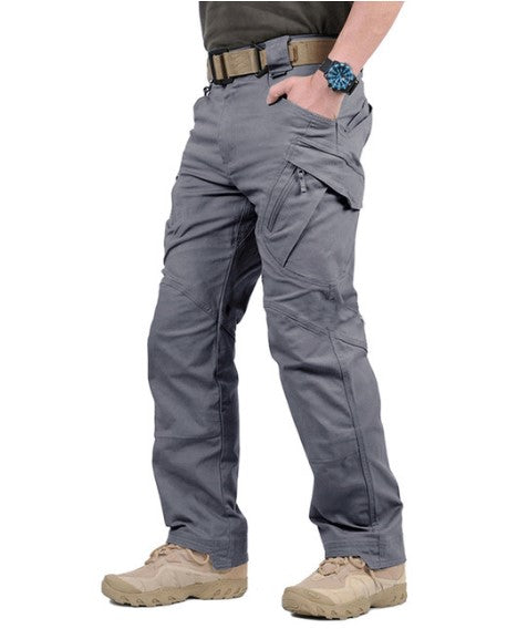 Grijze tactische broek met meerdere zakken, gedragen door man met beige schoenen en blauwe horloge. Ideaal voor outdoor en survival activiteiten.