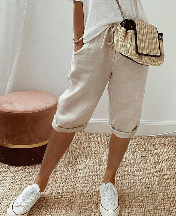 Vrouw in casual outfit met beige linnen shorts, witte sneakers en een geweven schoudertas. Perfect voor zomerse mode en comfortabele stijl.