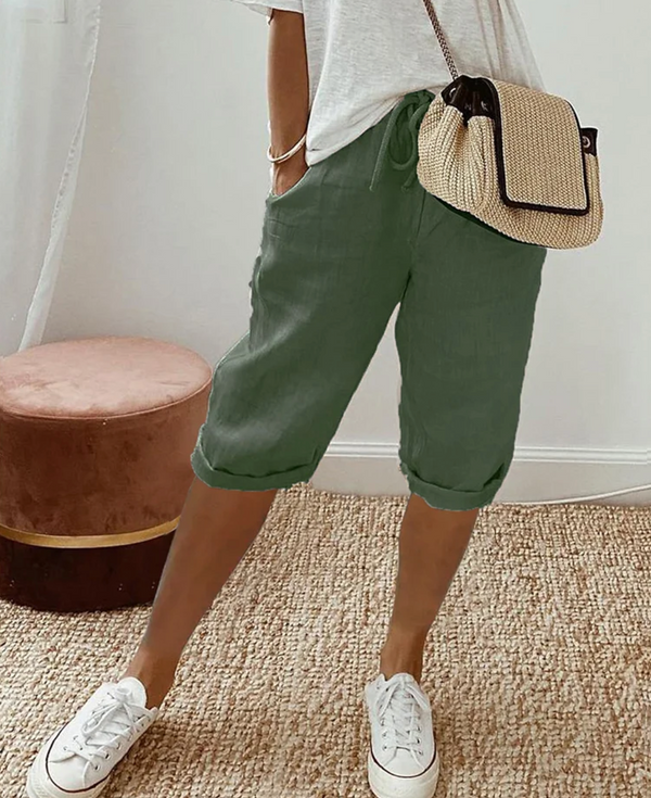 Vrouw in casual outfit met groene linnen bermuda, witte sneakers en een beige schoudertas. Stijlvolle zomermode, comfortabele kleding.