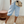 Vrouw in casual outfit met lichtblauwe linnen shorts, witte sneakers en een beige schoudertas. Perfecte zomermode, comfortabele en stijlvolle look.