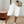 Vrouw in casual outfit met witte linnen bermuda shorts, beige schoudertas en witte sneakers op een beige tapijt. Perfect voor zomermode en comfort.