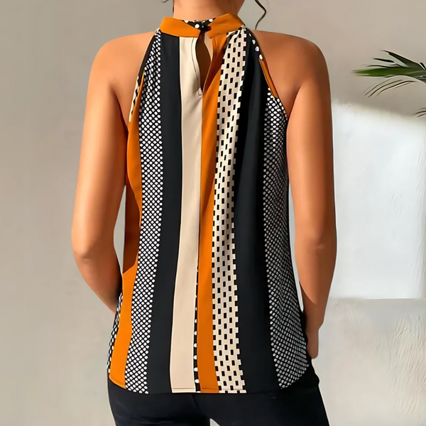 Vrouw in mouwloze top met zwart-wit geometrisch patroon en oranje strepen, staand voor een neutrale achtergrond. Modieuze dameskleding.