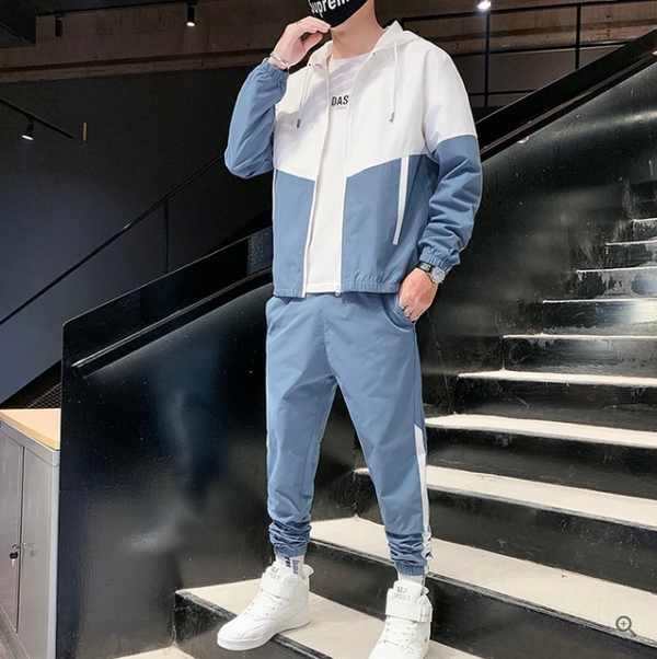 Man in blauw-wit trainingspak met capuchon en sneakers op zwarte trap. Stijlvolle sportkleding, casual outfit, moderne herenkleding.