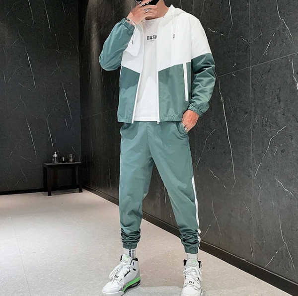 Man in groene en witte trainingspak met sneakers, staand in moderne kamer. Sportieve outfit, casual mode, herenkleding, streetwear stijl.