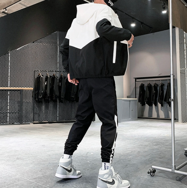 Man in zwart-wit sportkleding met capuchon en sneakers in moderne kledingwinkel. Stijlvolle herenkleding, urban fashion, sportieve outfit.
