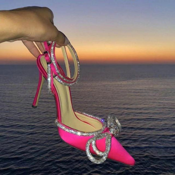 Roze hoge hak met strass, vastgehouden bij zonsondergang boven zee. Luxe damesschoen, opvallend design, elegante avondmode.