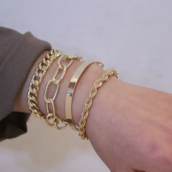 Gouden armbanden set op pols, inclusief schakelarmbanden en gladde bangle, stijlvolle sieradenaccessoires voor dames, modetrend 2023.