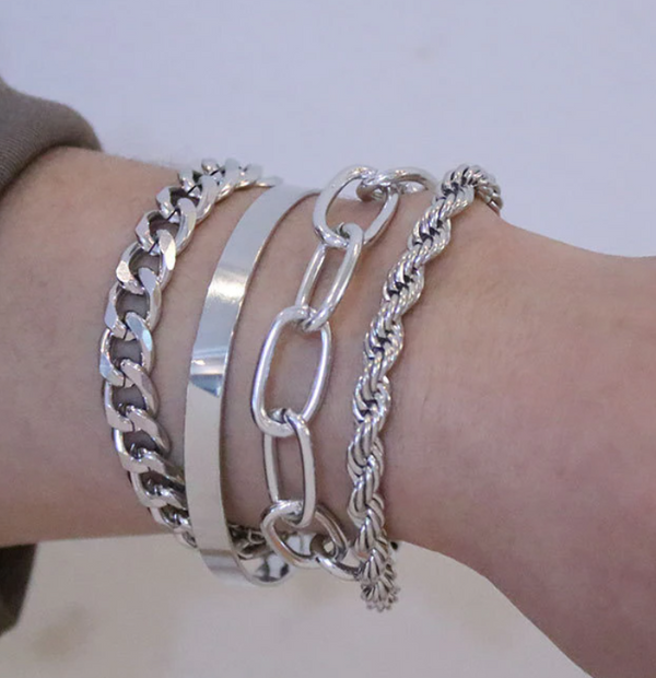 Pols met vier zilveren armbanden: schakelarmband, gladde armband, grove ketting en gedraaide armband. Modieuze sieraden voor dames.