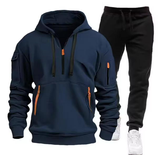 Donkerblauwe hoodie met rits en oranje accenten, gecombineerd met zwarte joggingbroek en witte sneakers. Comfortabele herenkleding set.
