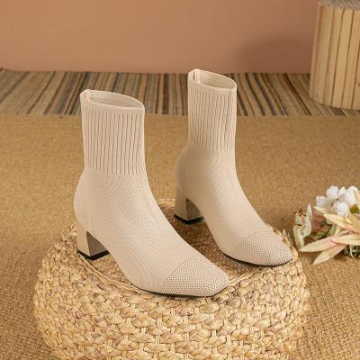 Beige enkellaarsjes met blokhak en geribbelde schacht op een gevlochten poef, omgeven door bloemen. Stijlvolle damesmode, herfstcollectie.