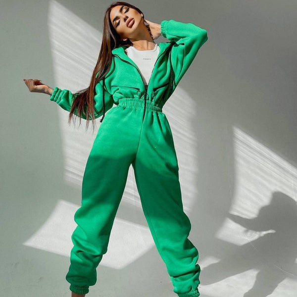 Vrouw in groene joggingpak poseert tegen witte achtergrond, modieuze sportkleding, comfortabele loungewear, trendy damesmode.