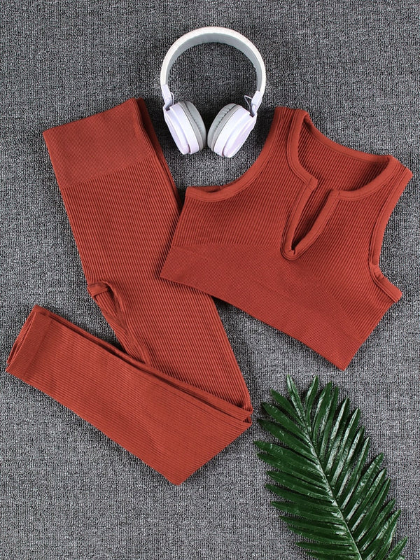 Bruin geribbelde sportset met top en legging op grijze achtergrond, witte koptelefoon en groene palmblad. Perfect voor yoga en fitness.