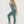 Vrouw in turquoise sportset, bestaande uit naadloze legging en sportbeha, poseert tegen witte achtergrond. Fitnessmode, actieve kleding.