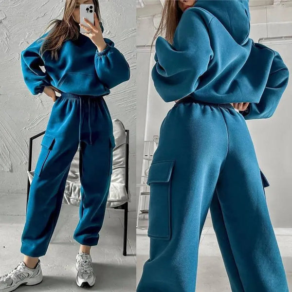 Vrouw in blauwe joggingpak met capuchon en cargobroek, comfortabele sportkleding, casual mode, trendy outfit, grijze sneakers, moderne stijl.