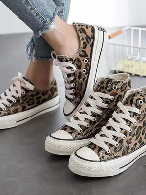 Luipaardprint sneakers met witte veters en rubberen zolen, gedragen door persoon in blauwe jeans. Modieuze casual schoenen voor dames.