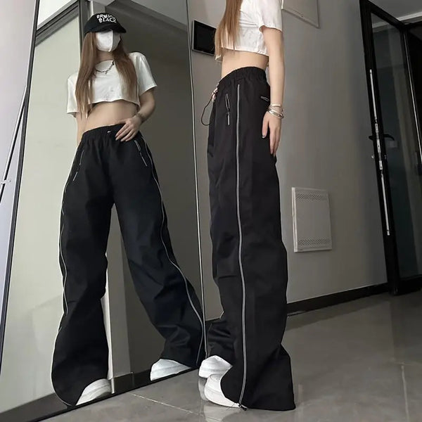 Vrouw in zwarte wijde broek en wit crop top voor spiegel, trendy streetwear mode, casual outfit, lange broek met rits, modeaccessoires.