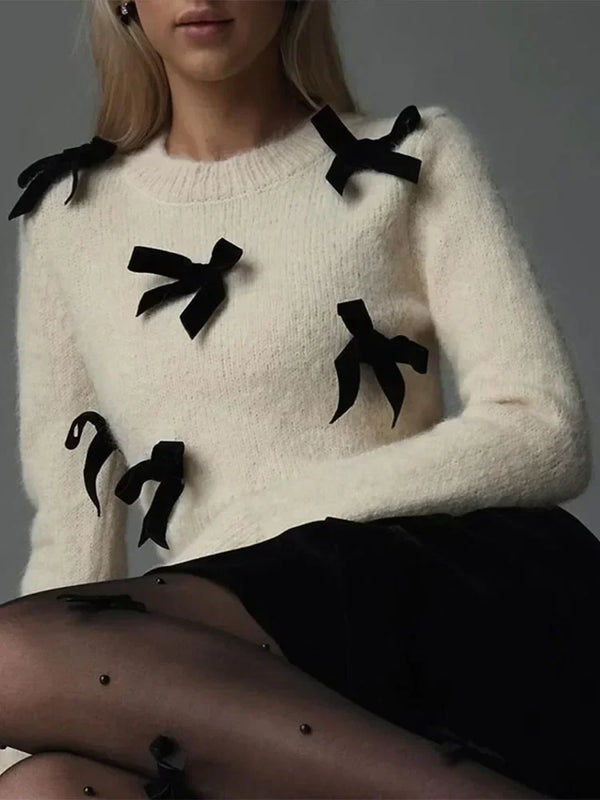 Vrouw in crèmekleurige trui met zwarte strikjes, zittend in zwarte rok en doorschijnende panty. Modieuze dameskleding, herfst/winter stijl.