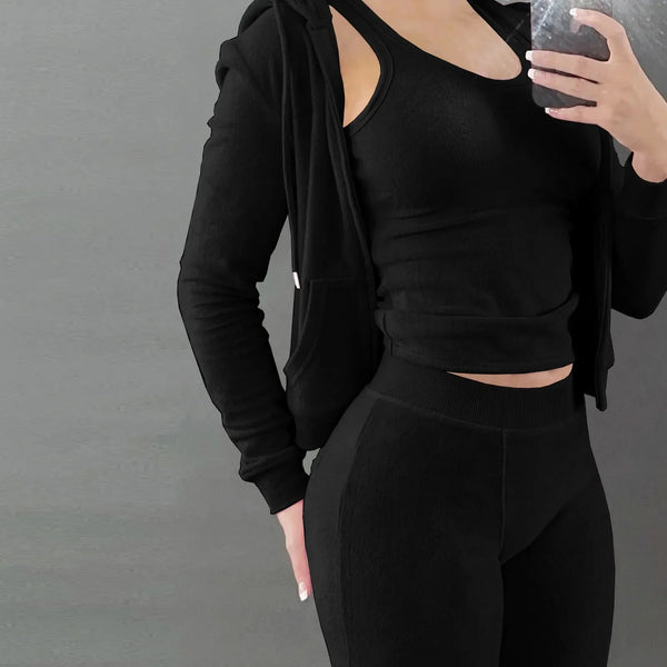 Vrouw in zwarte sportkleding, bestaande uit een tanktop, legging en hoodie, tegen een grijze achtergrond. Fitnessmode, actieve levensstijl.