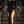 Elegante vrouw in zwarte fluwelen avondjurk met hoge split, gouden clutch en oorbellen, poseert op trap. Luxe mode, avondkleding, glamour.