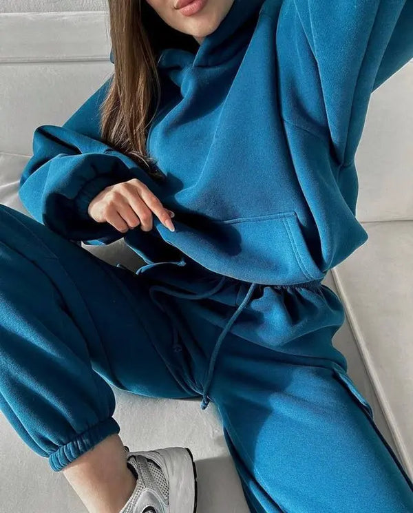 Vrouw in blauwe hoodie en joggingbroek op witte bank, casual mode, comfortabele loungewear, trendy sportkleding, relaxte stijl.