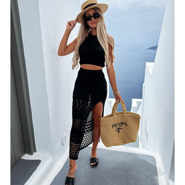 Vrouw in zwarte zomerjurk met hoed en zonnebril, draagt een Prada rieten tas. Stijlvolle vakantielook op zonnige dag in Santorini, Griekenland.