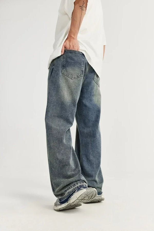 Man in losse, vintage blauwe spijkerbroek en witte sneakers, casual mode, streetwear stijl, witte achtergrond, trendy herenkleding.